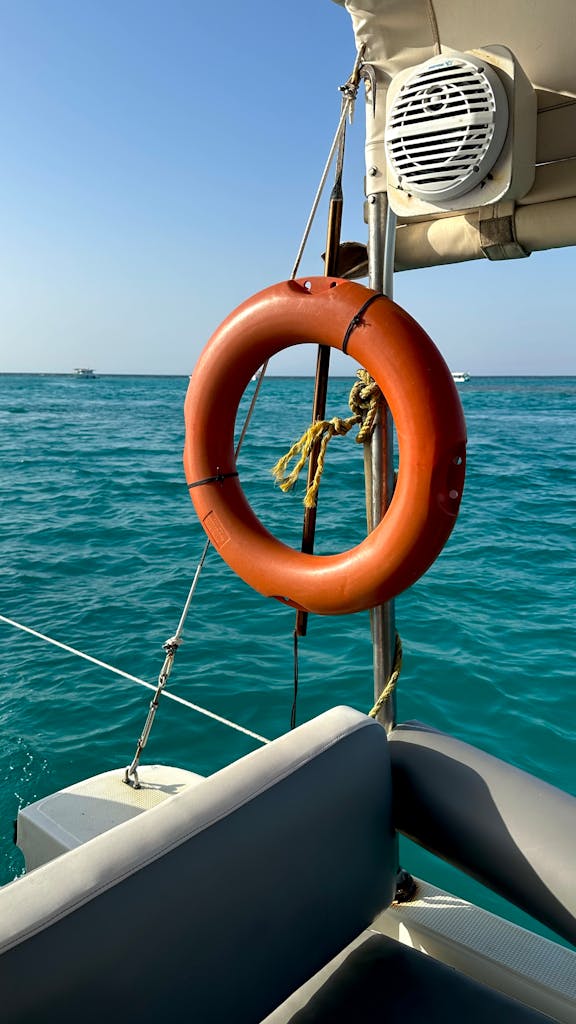 Bright orange life buoy hanging on a boat amidst clear blue ocean waters, sunny weather.